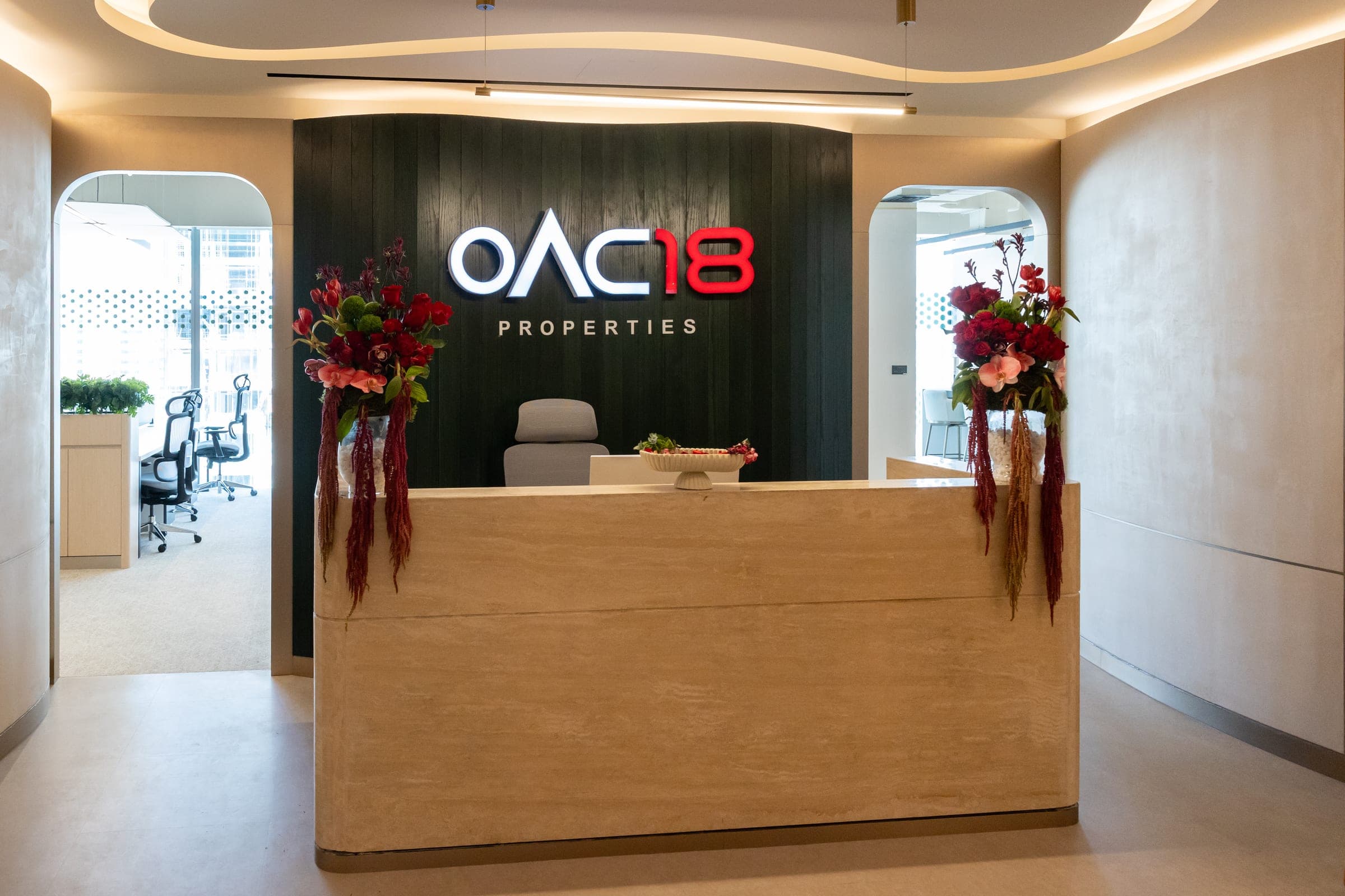 Photograph of the OAC18 Properties reception at The Opus, Business Bay, with the OAC18 sign on a dark panelled wall and flowers either side of the desk