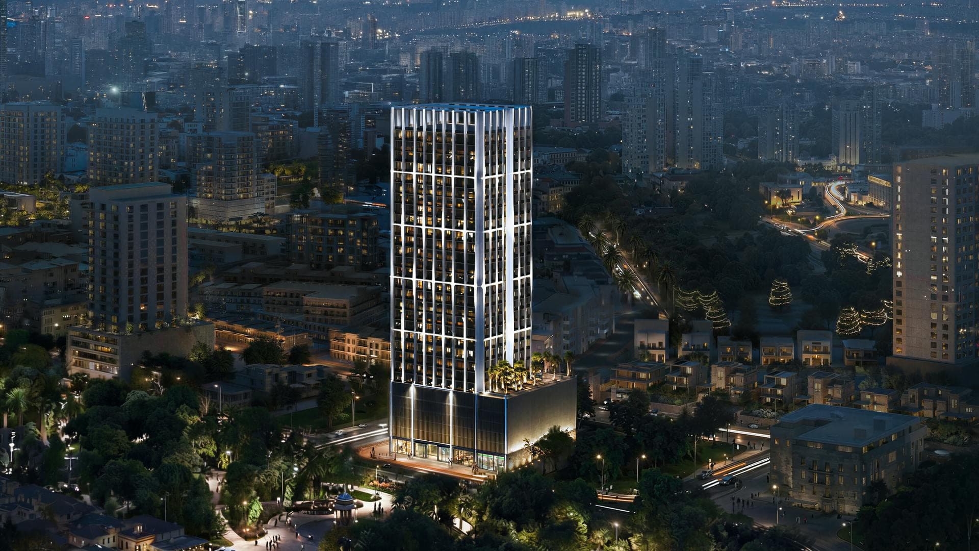 Render of Binghatti Etherea in Jumeirah Village Circle at night from the air, the tower's lit vertical frames rising above tree-lined streets and low-rise houses