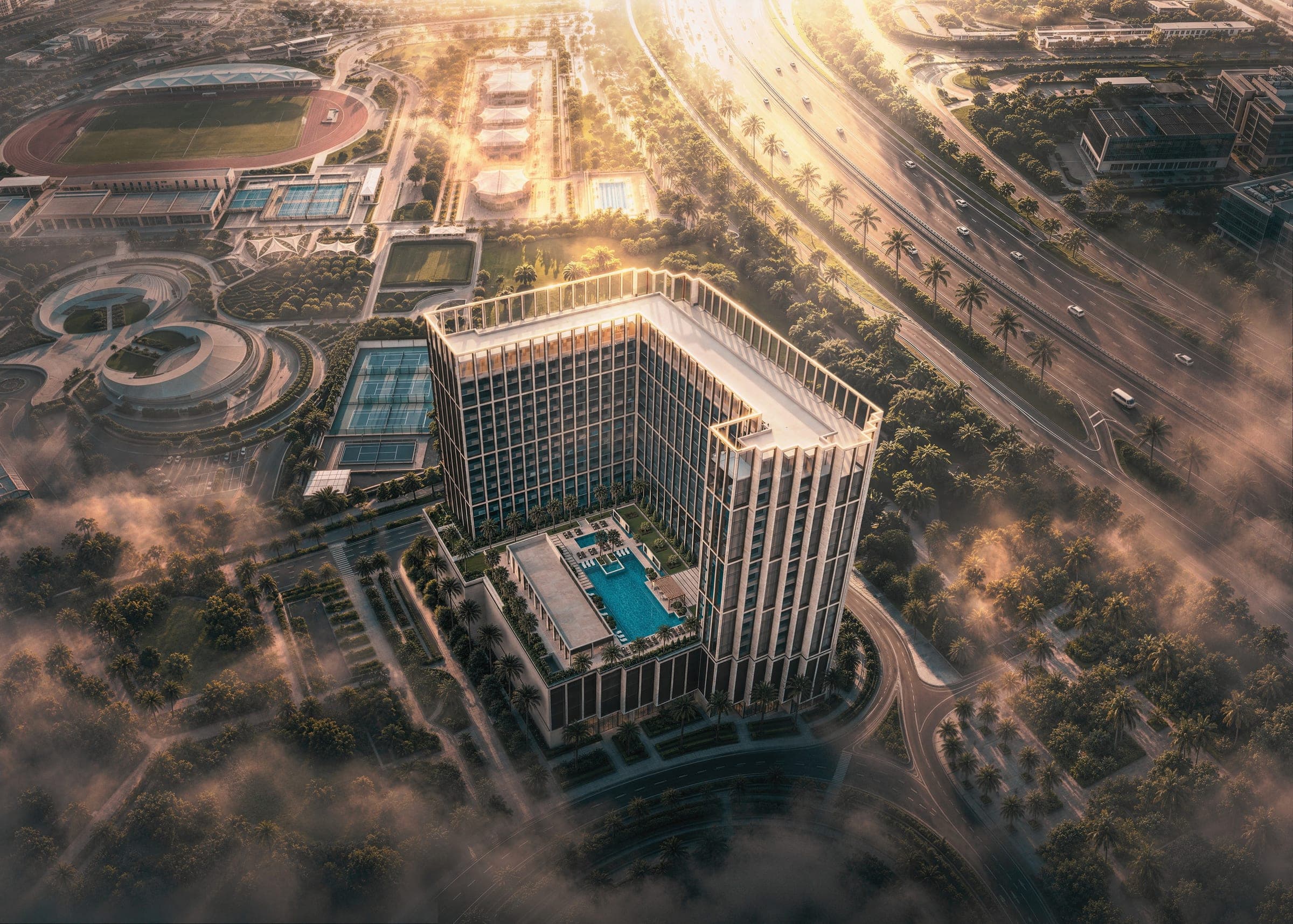 Render of Binghatti Starfall from the air in low golden sun, the L-shaped building set around a podium pool deck, beside a highway and sports grounds