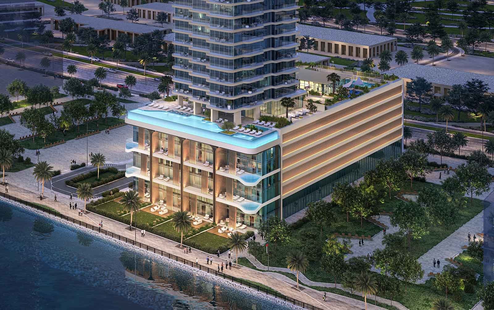 Render of the podium of LIV Maritime at Dubai Maritime City from the air at dusk, a lit rooftop pool and glazed balconies above the waterfront promenade