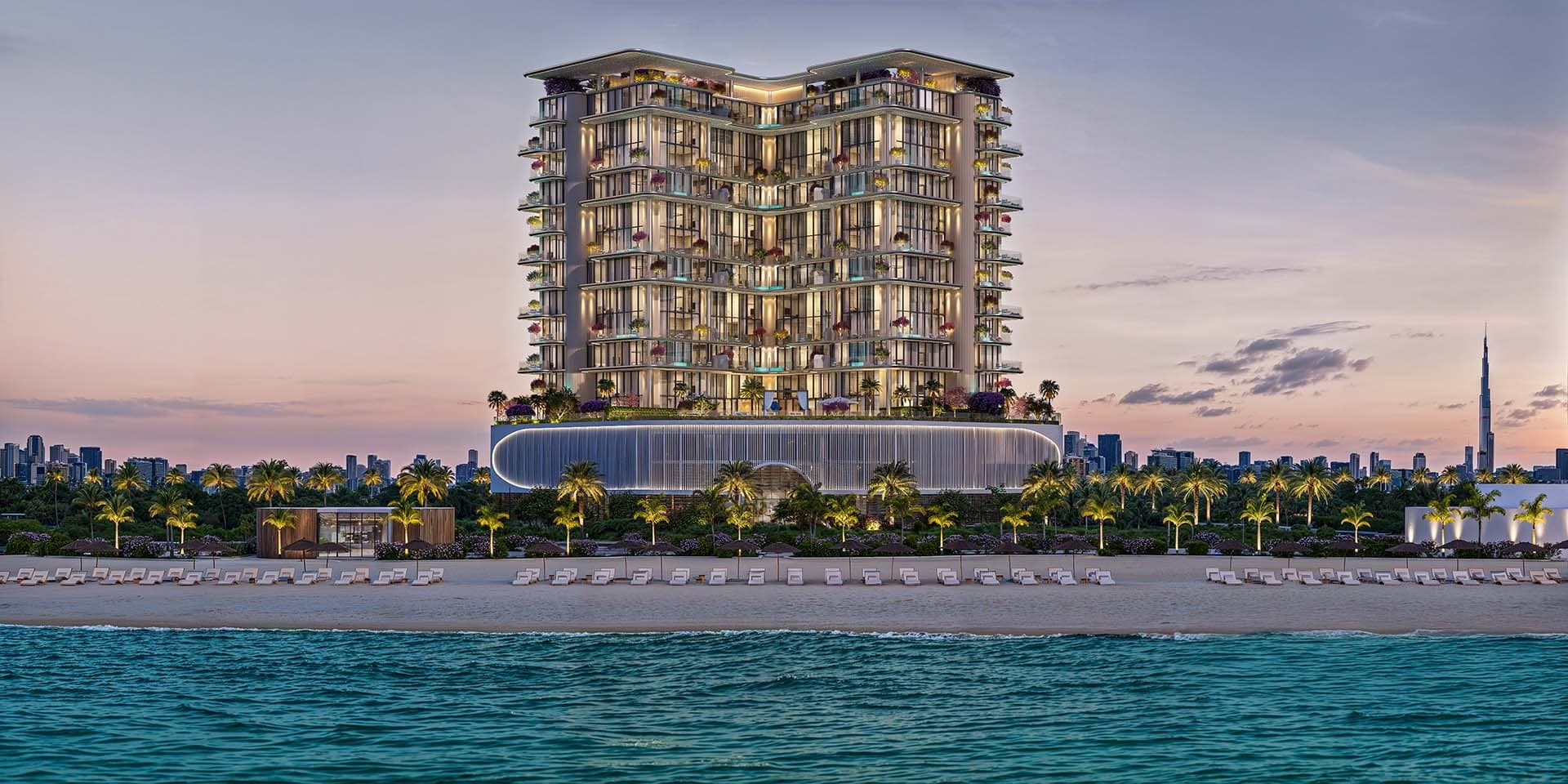 Render of Villa del Gavi on Dubai Islands at dusk seen from the sea, a lit terraced building on a fluted podium behind palms and a beach of loungers