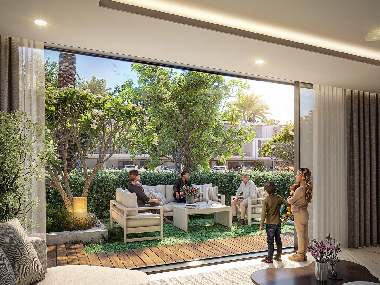 Render of a Violet 4 townhouse living room with a full-width glass opening onto a garden where three adults sit on outdoor sofas and two children watch from inside, with neighbouring townhouses and parked cars beyond the hedge